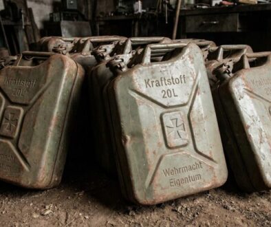 Row of rusty 20L fuel cans labeled Kraftstoff, Wehrmacht Eigentum, in a dusty workshop setting.