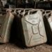 Row of rusty 20L fuel cans labeled Kraftstoff, Wehrmacht Eigentum, in a dusty workshop setting.