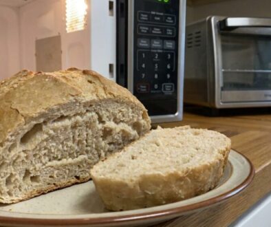 Loaf of crusty bread on a plate in a kitchen, with a toaster oven and microwave in the background.