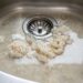 Rice clumps soaking in a stainless steel kitchen sink around the drain