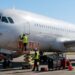 Ground crew in high-visibility vests servicing a large white commercial airplane on the tarmac with a maintenance lift nearby.