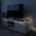 Living room setup with a large TV on a white media console, along with gaming consoles and a router, plugged into glowing power strips on the wall.