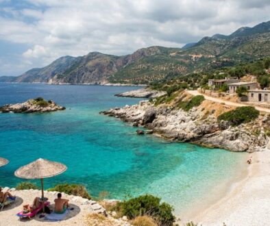 Turquoise cove with a sandy beach, thatched umbrellas, and sunbathers along a rocky coastline.